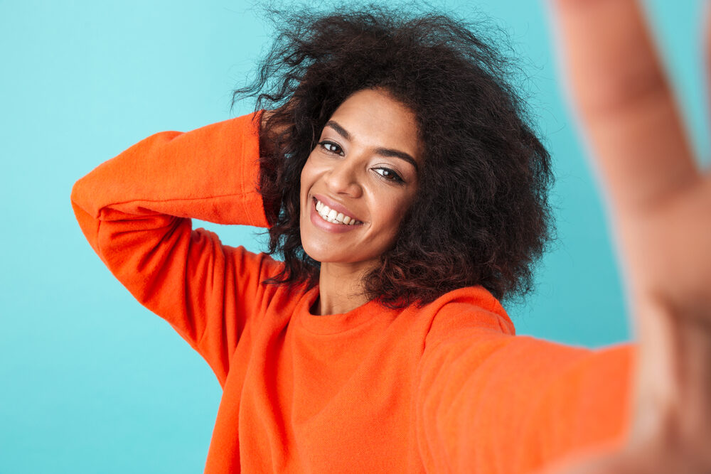 Joyful African American female with healthier hair after using Olaplex to repair hair damage.