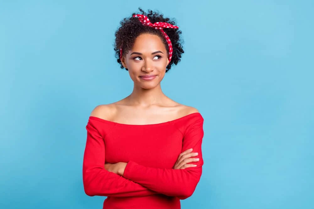 A beautiful light-skinned lady with 3B natural hair with her arms crossed while wearing a red shirt.
