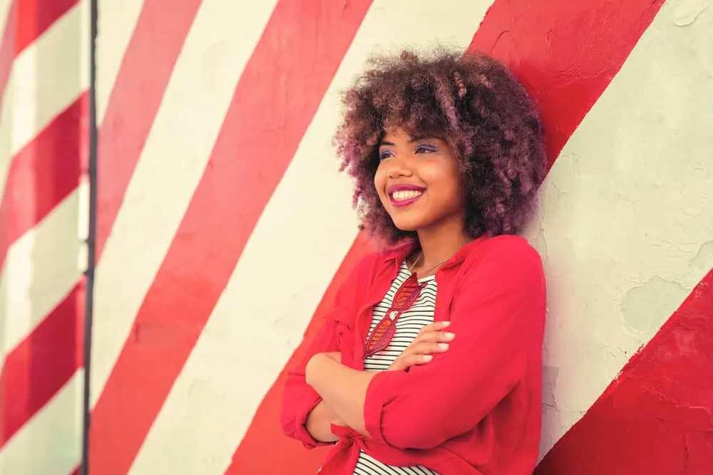How To Stop Hair Dye From Bleeding and Dyes That Don’t Bleed 6 Positive young black woman with curly healthy hair dyed multiple colors soaking up the sun's UV rays outdoors.