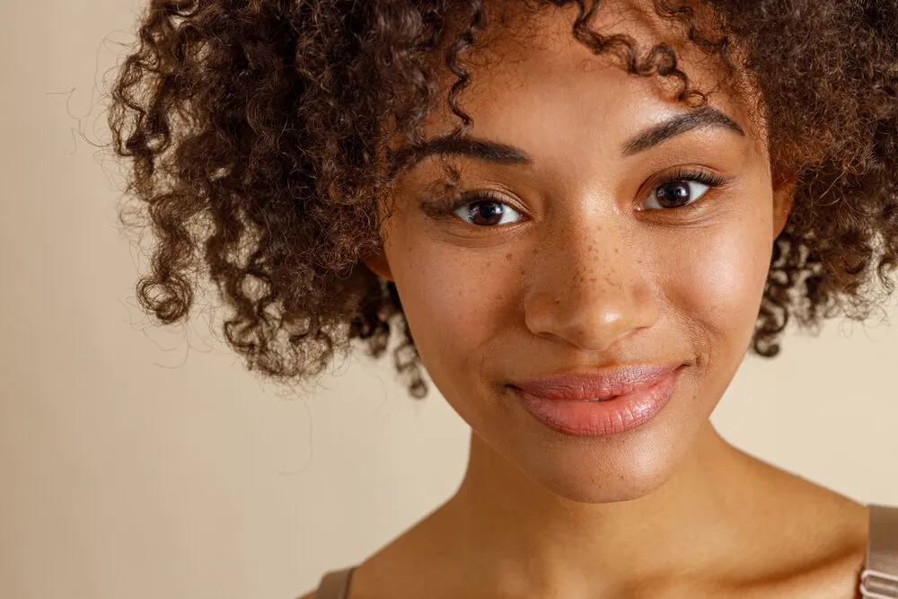 Is Volume Powder Bad for Your Hair? What Is It? Is It Safe? 6 Young African American girl with freckles on her nose wearing curly 3C natural hair.