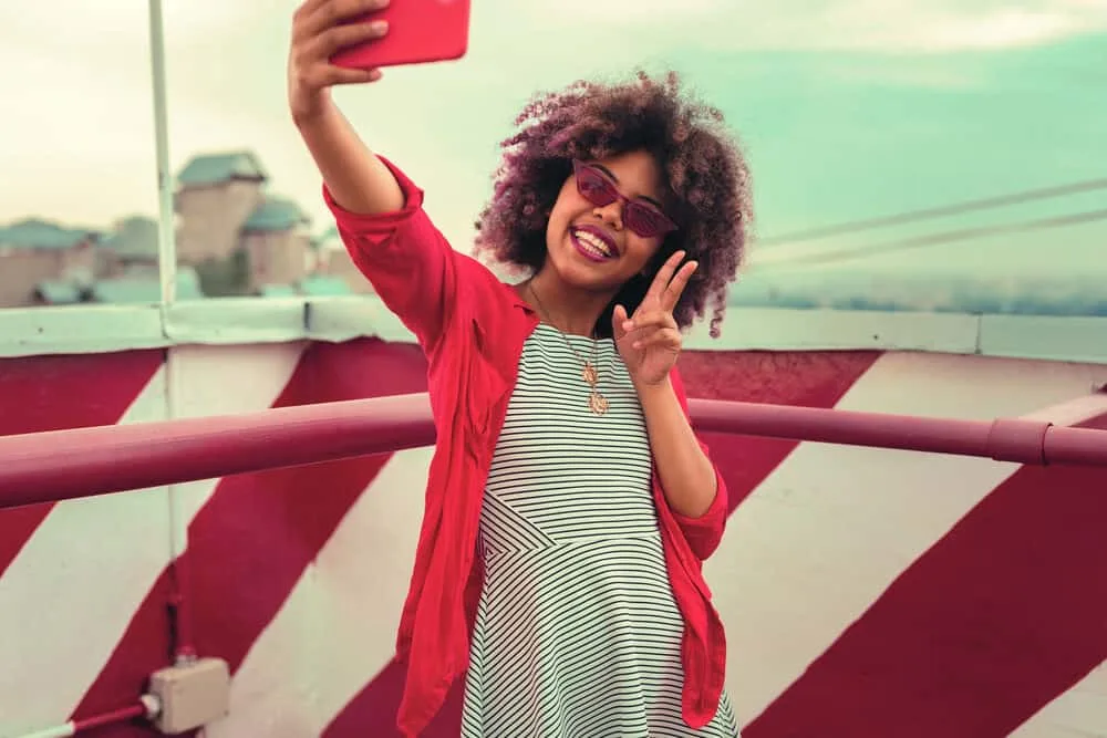 A cheerful African American female with color-treated hair takes a selfie after using color-safe shampoo.