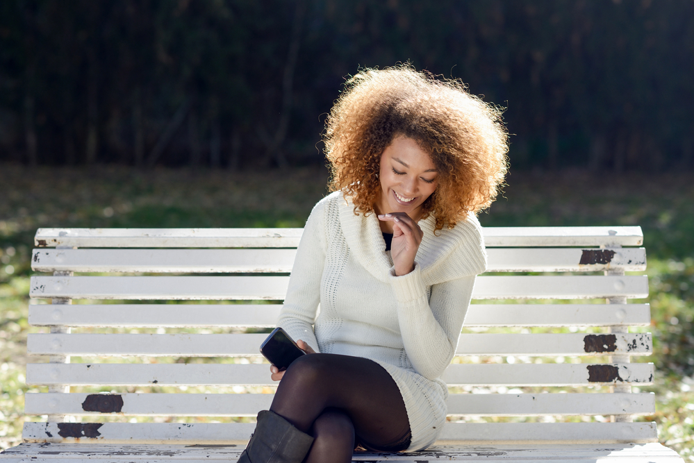 Beautiful black girl with bleached hair enjoying her time outside while sitting on a painted park bench.