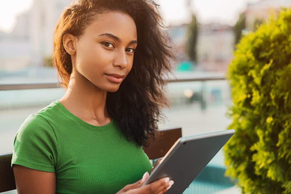 African American female with heat-damaged hair researching how to care for delicate strands using her tablet.