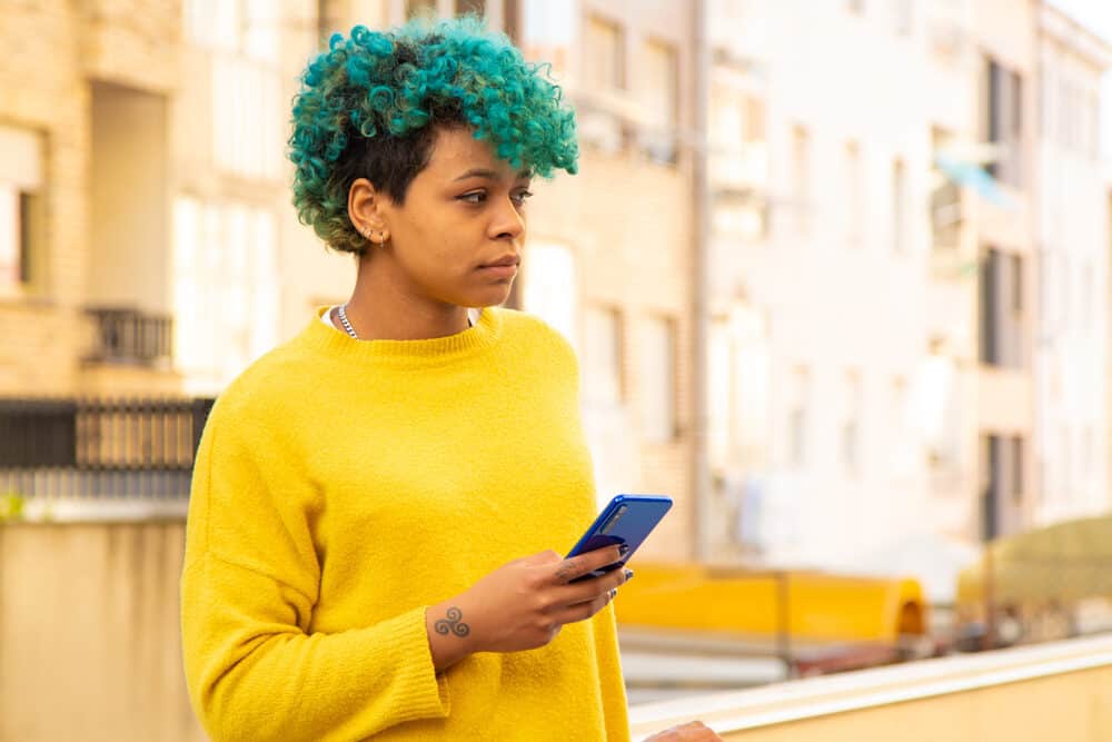 Young lady with 3A curls colored with blue hair dye wearing a silver necklace and yellow sweater.