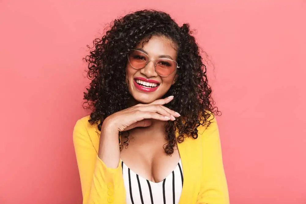 Is Curly Hair Attractive? Why? What Do Guys Think? 6 Lovely African female wearing a low-maintenance hairdo with a yellow jacket and pink-tinted glasses.