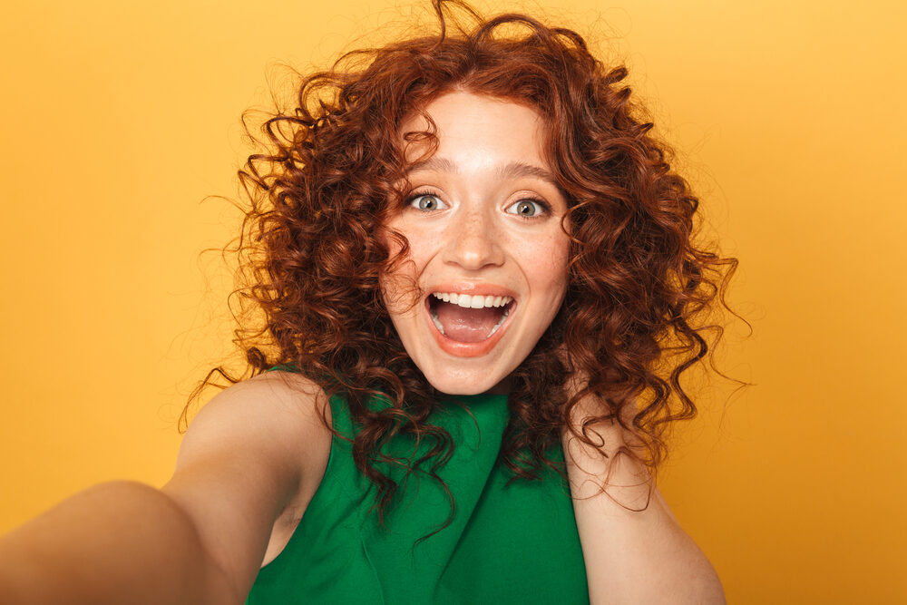 A female wearing a green dress with bouncy curls after using perm cream and a wide-toothed comb to style her hair.