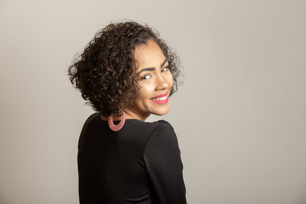 African American female with curly hair strands wearing pink hoop earrings and red lipstick.