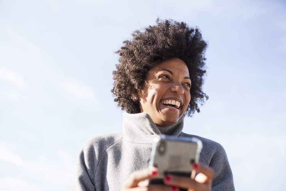 Cute black girl with beautiful skin and hair using an iPhone to text a friend in the park. 