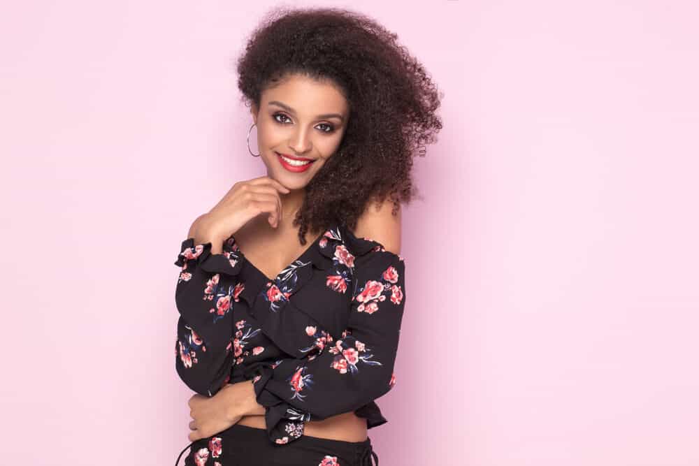 Beautiful African American female with a curly hair structure posing after getting hair lightening services.