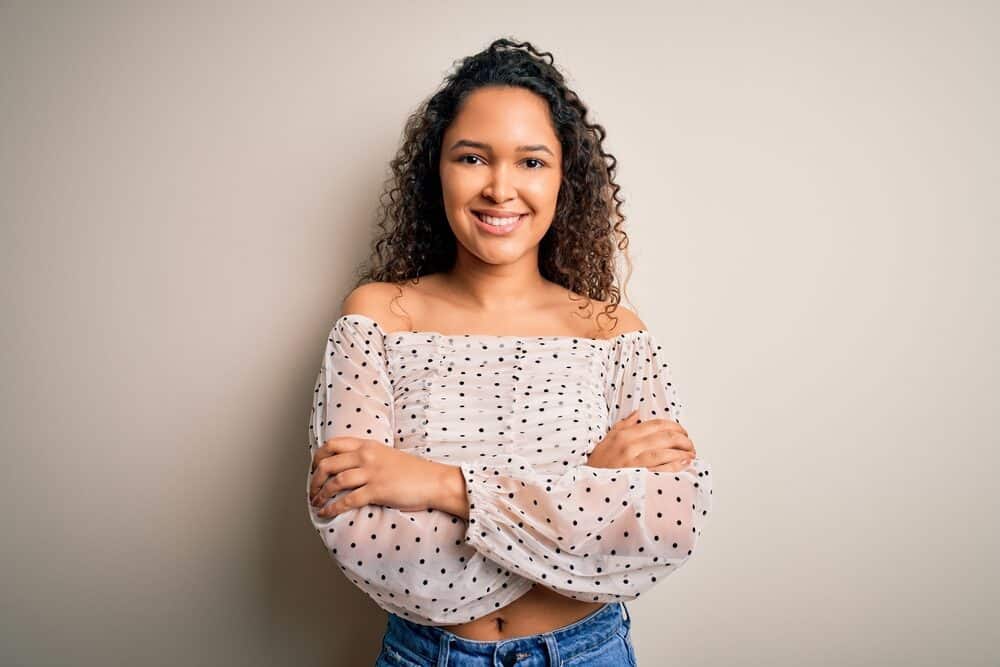 A beautiful woman with a deva hair cut wearing her curly natural hair with a black and white satin shirt.