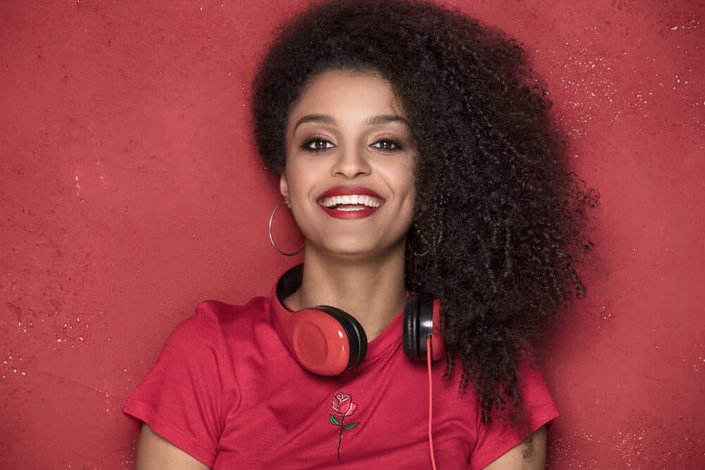 A black lady with natural curl definition and medium hair thickness wearing a red t-shirt and hoop earrings.