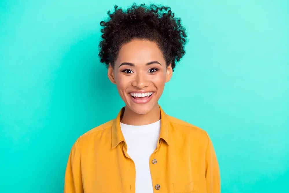 A woman wearing a yellow shirt with a great smile and natural curls ensures that she gets enough biotin from taking the recommended dosage.