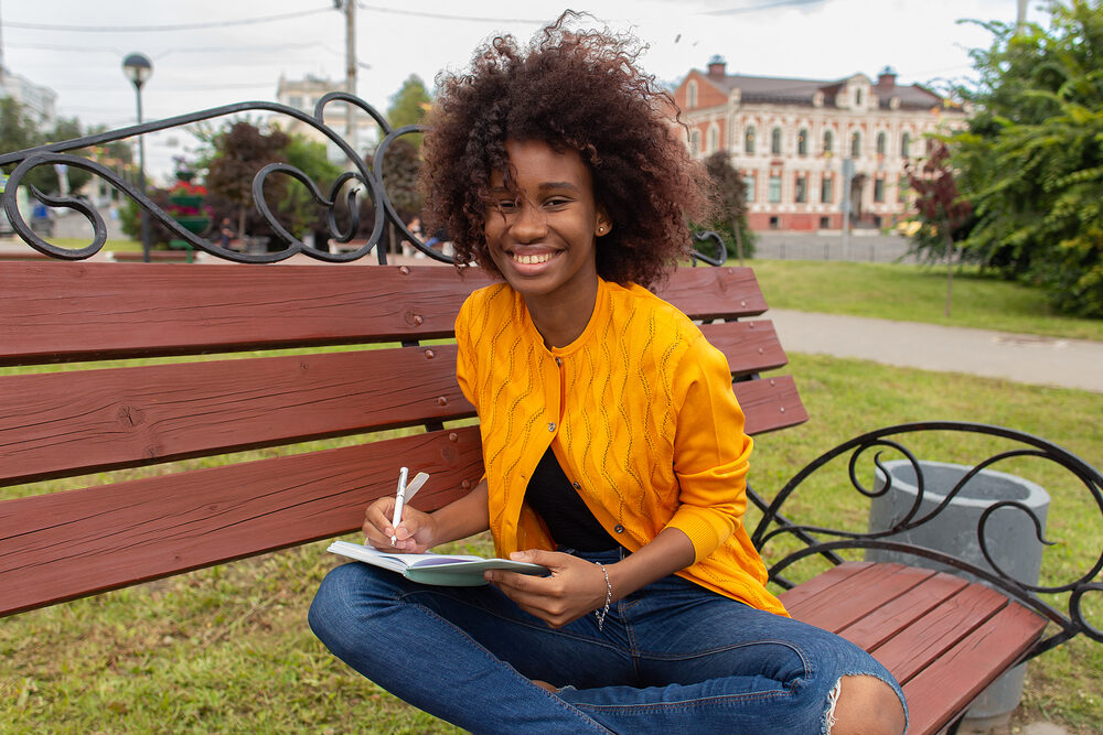 Young college student in the park with chronically dry hair soaking up the sun's UV rays while journaling.