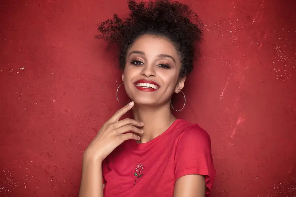 Should You Brush Curly Hair? Wet or Dry? Everyday? Before Bed? 4 Female with coily hair wearing a wash and go hairdo with red lipstick, hoop earrings, and pink eyeshadow.