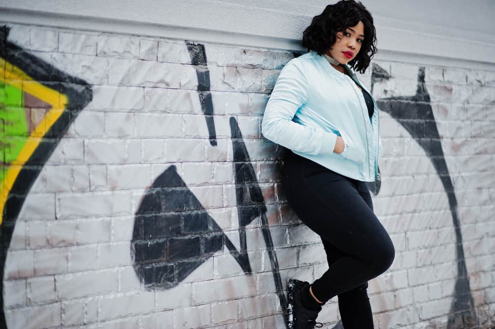 Hip black woman with a chin-length bob and red lipstick standing against a graffiti wall.