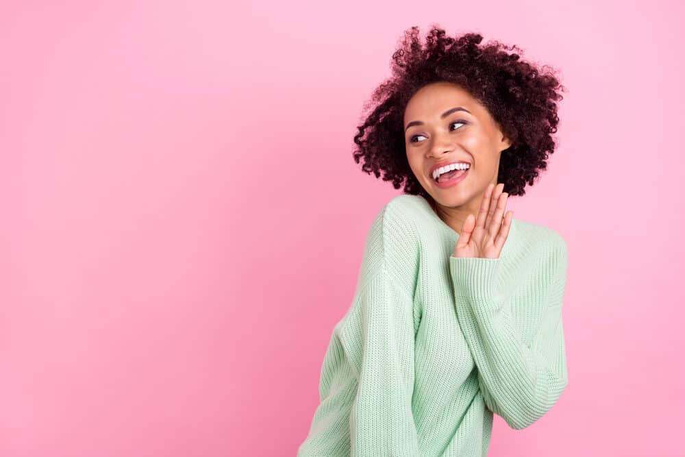 How To Dye Brown Hair Red With and Without Bleach at Home 3 Black girl with color-treated hair dancing while wearing a light green sweater and natural-looking make-up.