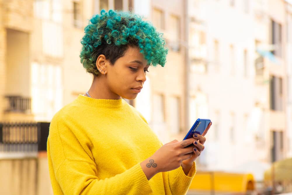 Cute young woman researching how to remove hair dye on her mobile phone.