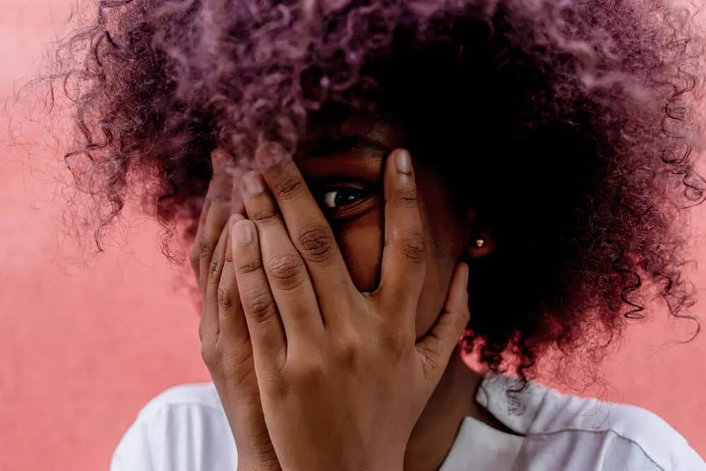 Is It Better to Dye Clean or Dirty Hair To Get the Best Results? 1 African American female with freshly washed hair covers face with hands.