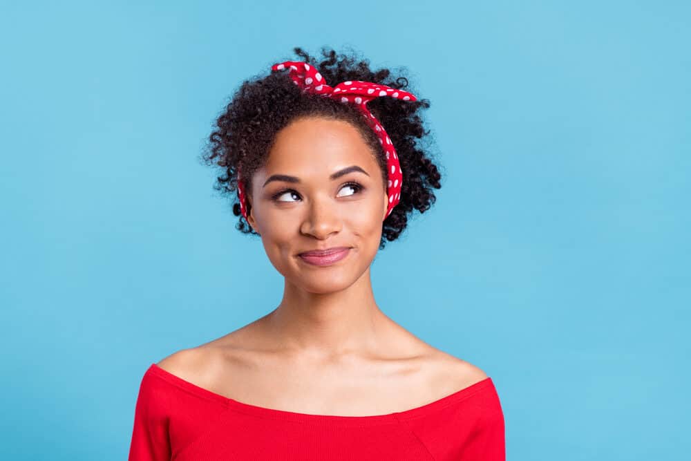Dreamy African American female with curly dry hair wearing a red and white polka dot hair tie.