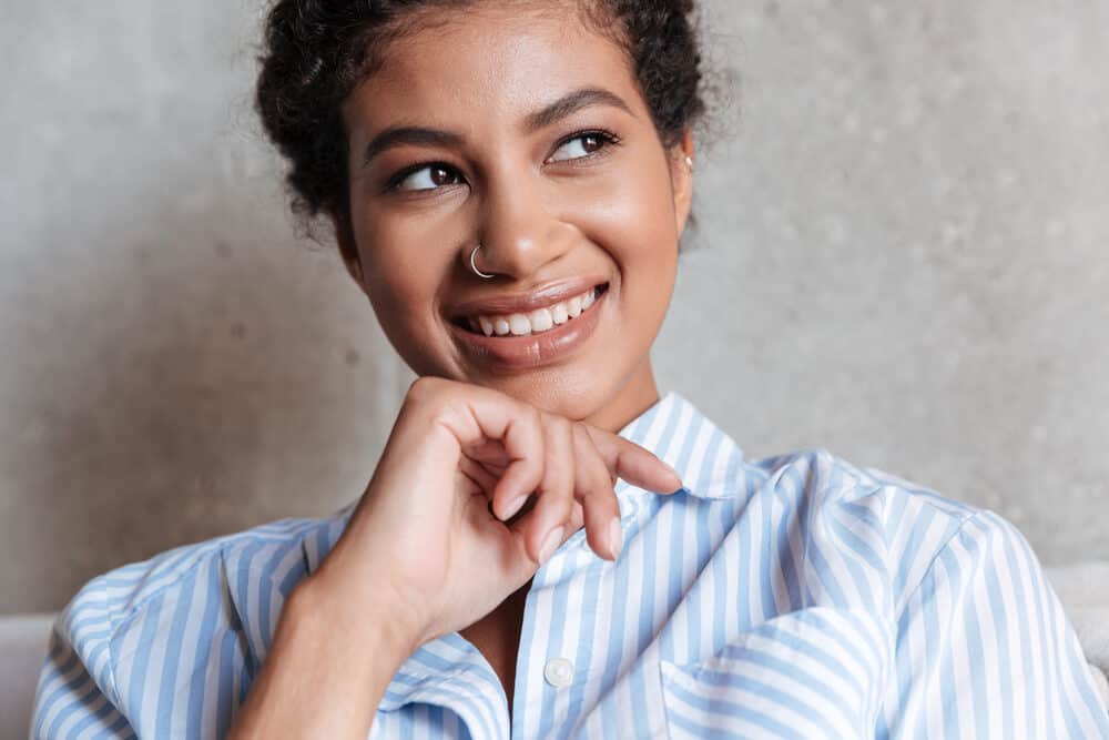 Lady wearing a blue and white shirt with naturally curly hair considering box color but worried about her hair health.