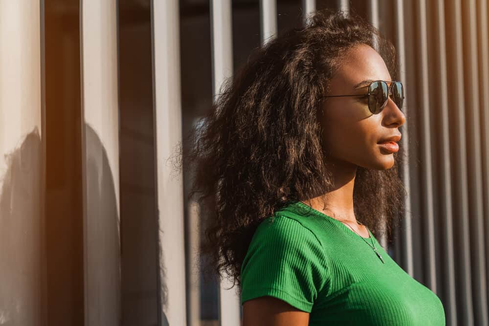 Stunning African American woman with straight hair wearing a gold necklace and black sunglasses.