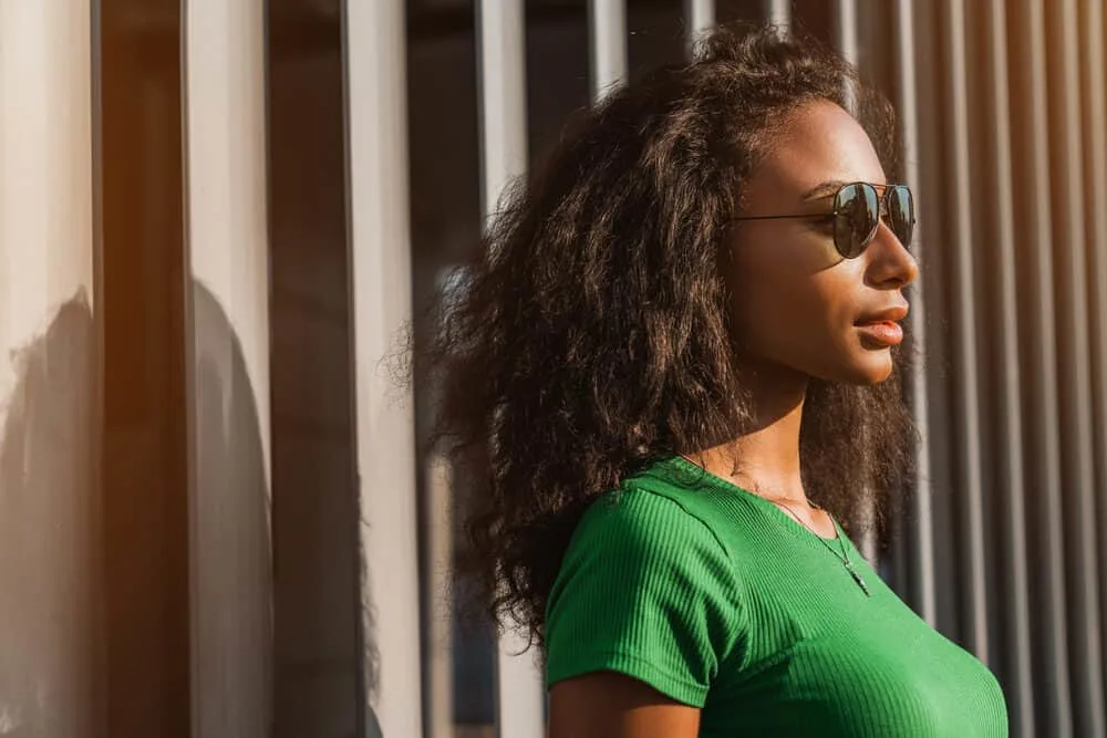 Stunning African American woman with straight hair wearing a gold necklace and black sunglasses.