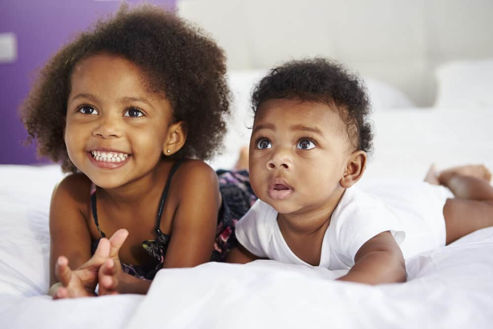 Two sisters with long hair watching television - one kid is 3 years old and the other is 40 weeks.