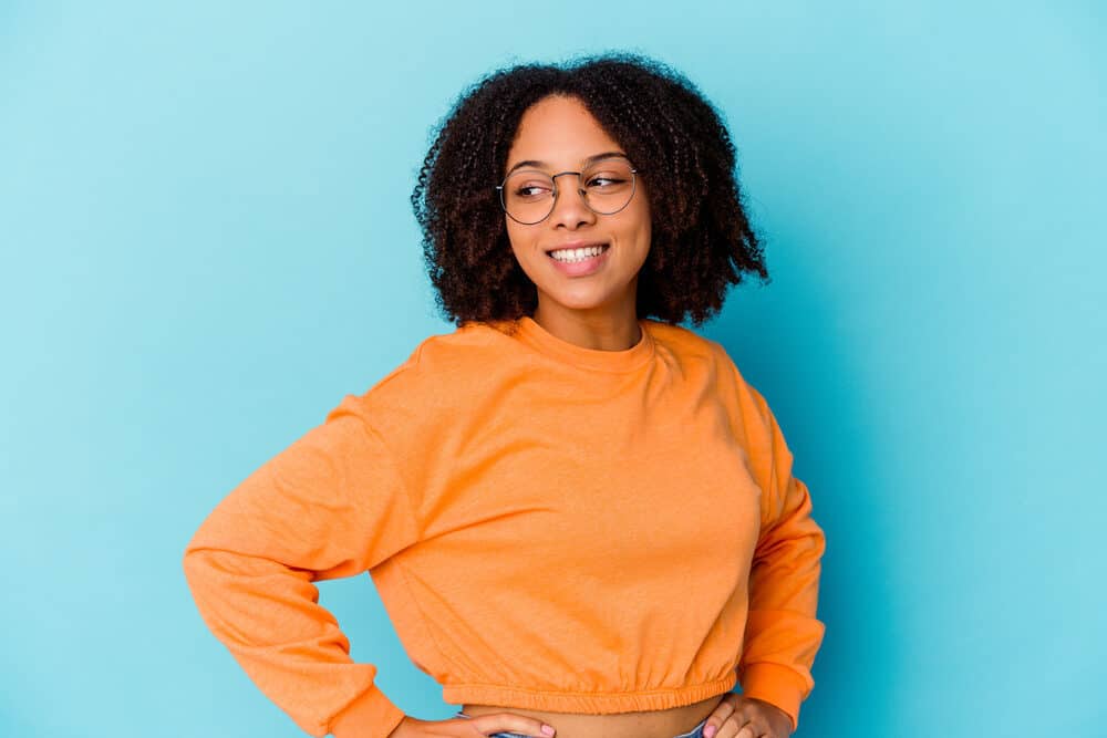 A black woman with thinning hair wearing a casual outfit with pink lipstick and round eyeglasses.