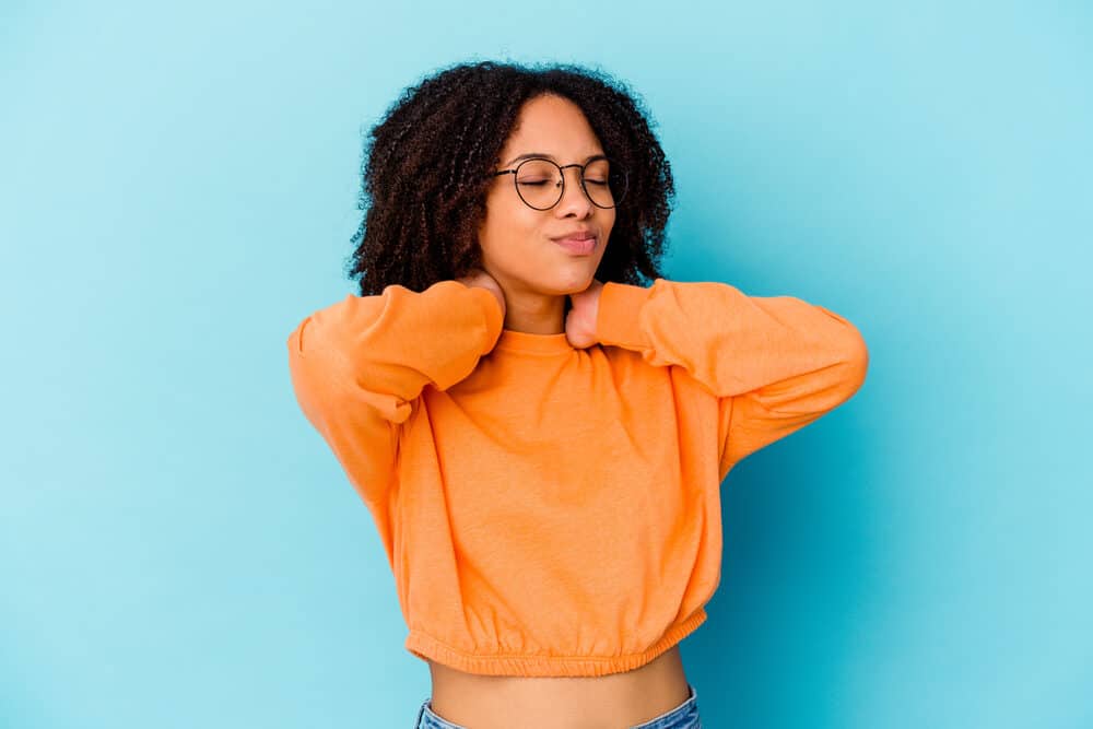 Young black with natural curls styled with Irish moss gel wearing a casual orange sweater and blue jeans.