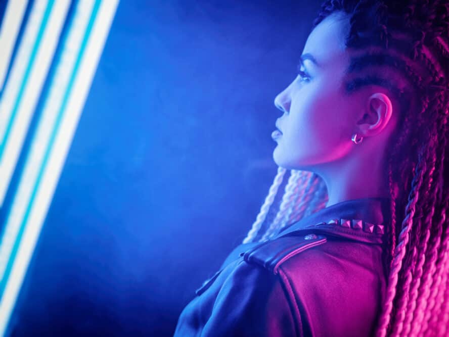 Side shot of a young lady wearing cornrow braids with gold earrings and a leather jacket.