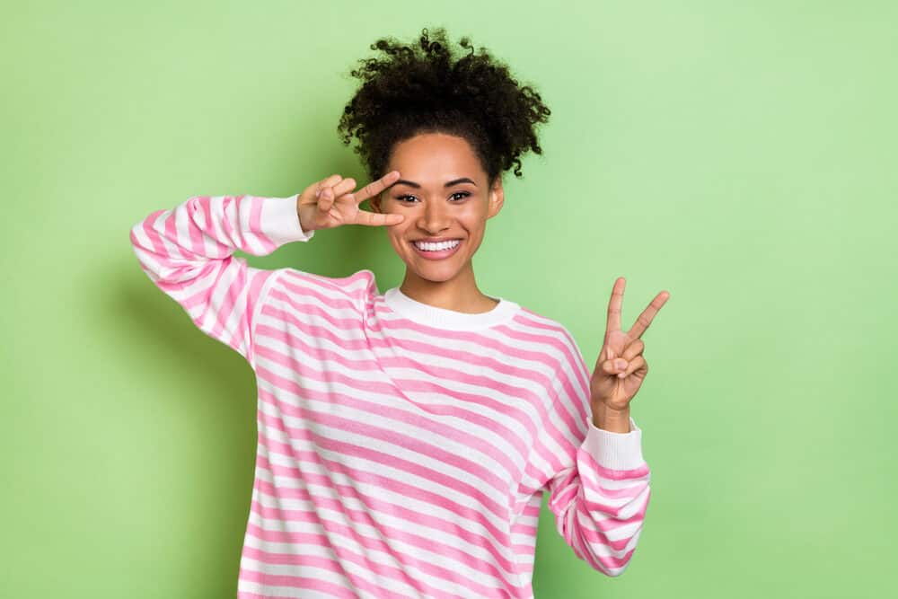 African American female dressed in a pink pullover with compromised hair and split-ends from dyeing her curls.