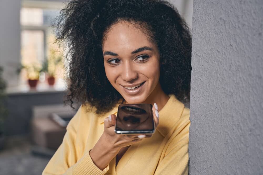 Young woman with curly hair using her iPhone to talk with a friend about using hair dye on kinky curly hair.