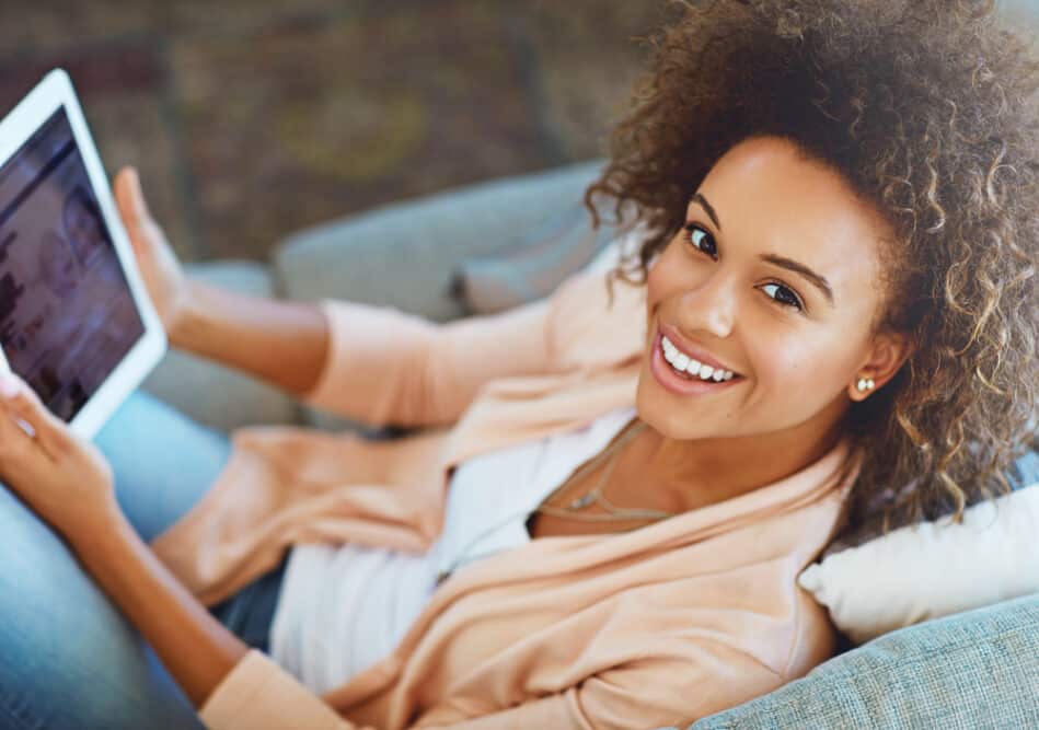 Black female sitting on her sofa relaxing while researching how to cover grey hair with permanent hair dye.