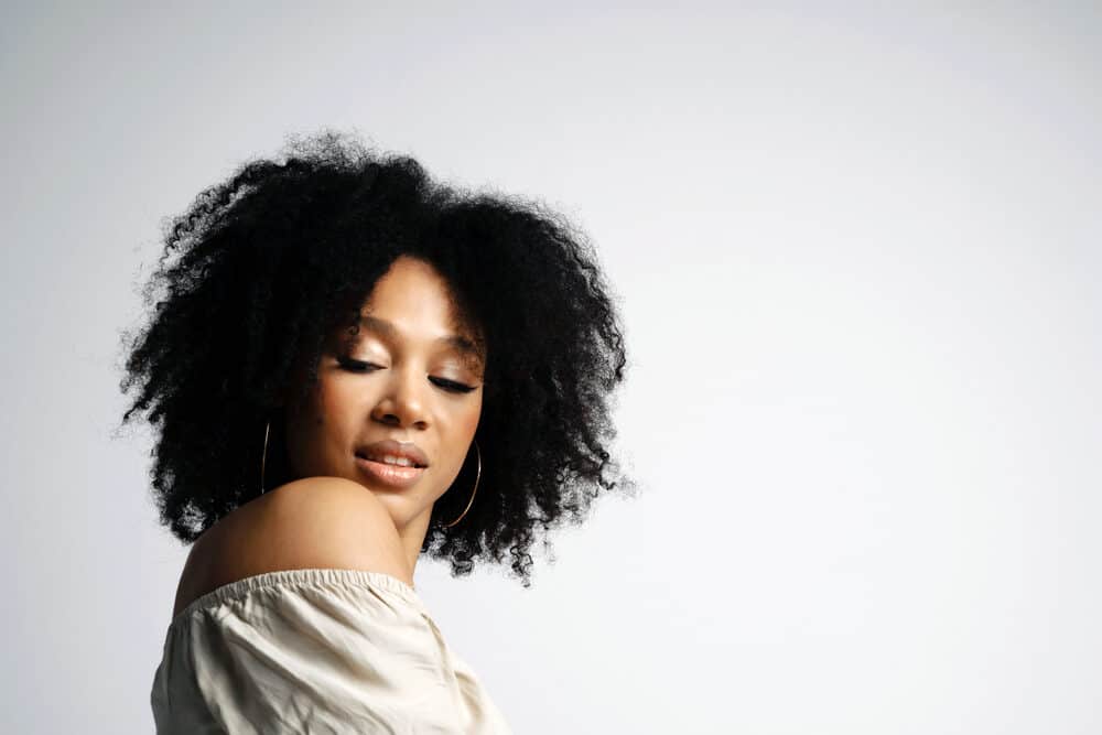 A female wearing an off-the-shoulder shirt with gold earrings wearing a wash n go style without harsh chemicals.