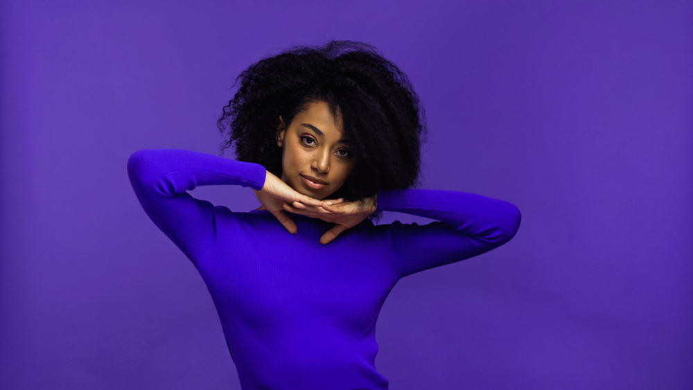 Beautiful black woman with caramel skin wearing a purple shirt and subtle pink lipstick.