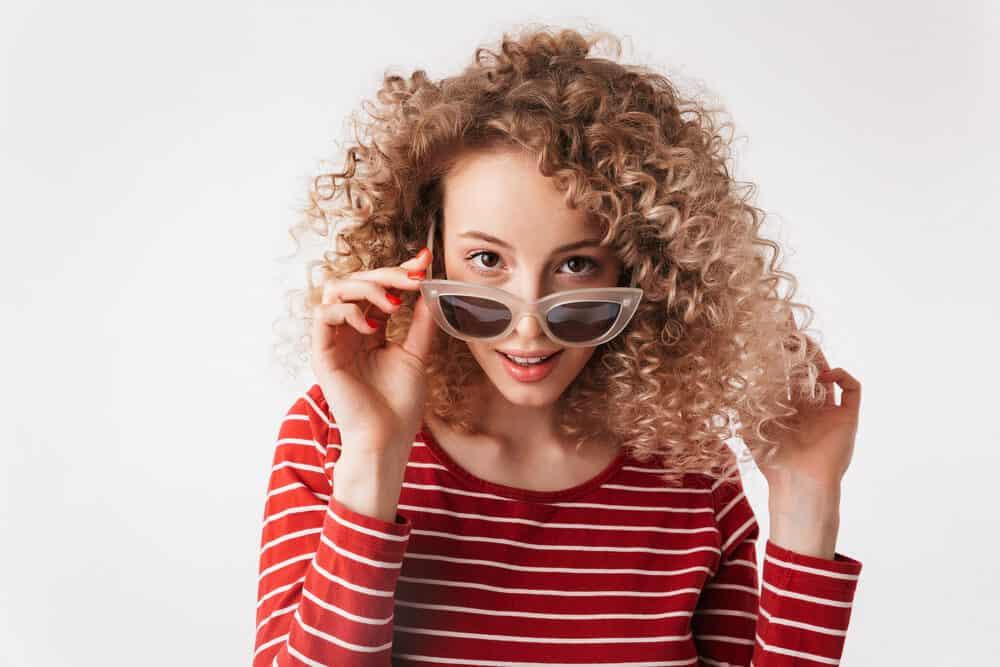 Stunning white female wearing her newly permed hair loose while posing with playful sunglasses.