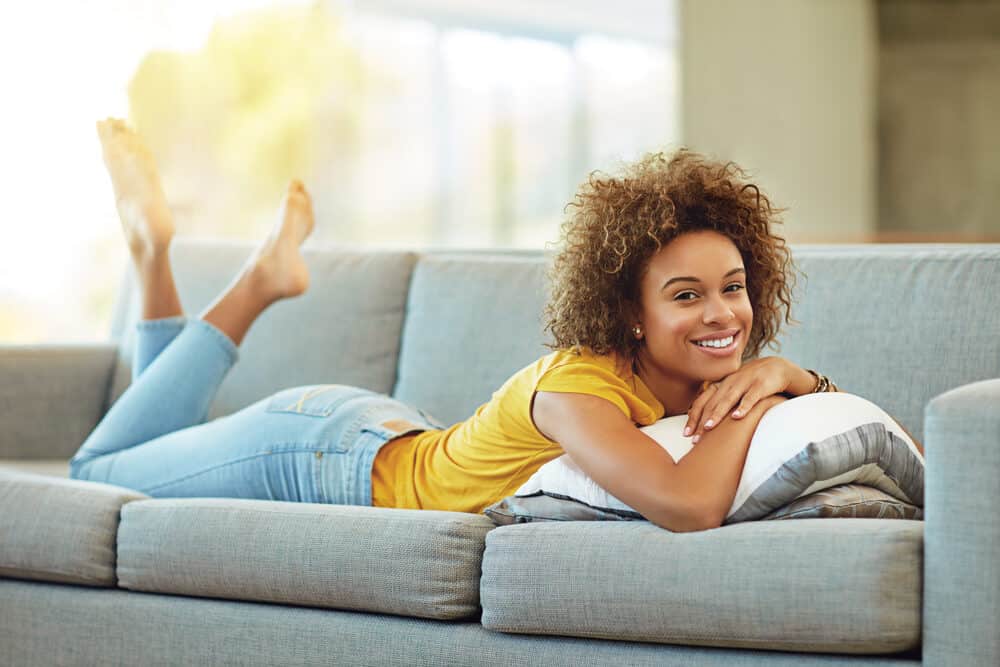 Cute adult female relaxing on the couch at home wearing casual clothes and brown hair dye in a wash n go style.