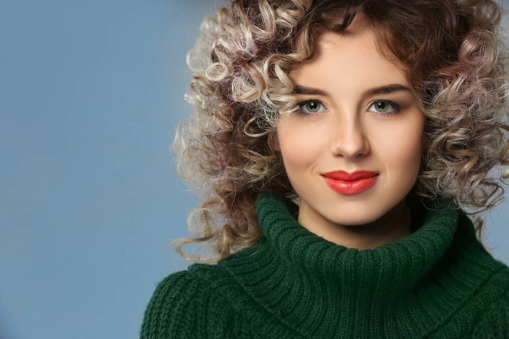 Beautiful young woman with beachy waves on shoulder hair length wearing a green sweater and red lipstick.