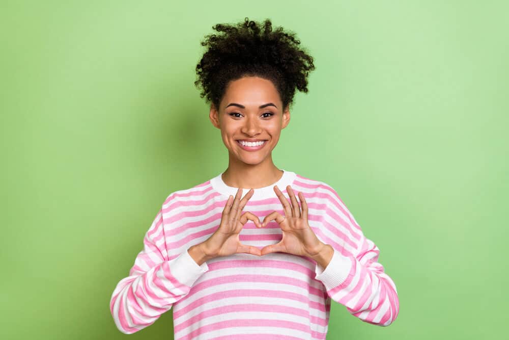 A woman with light caramel skin smiling after getting healthier hair after using an Olaplex treatment.