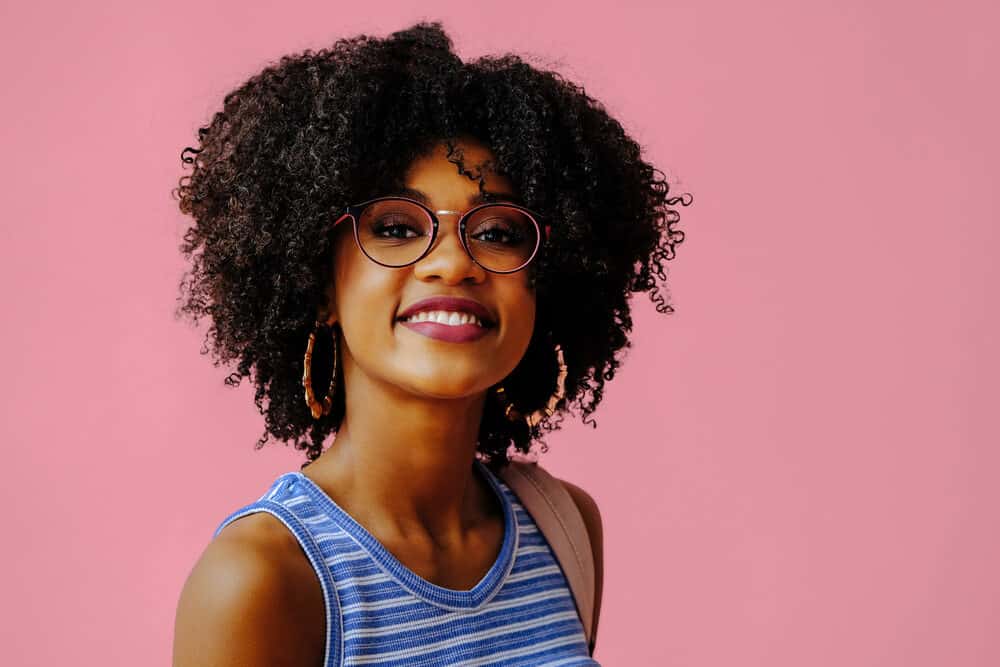 Cute African American female with a full head of curly thick hair strands wearing black eyeglasses.