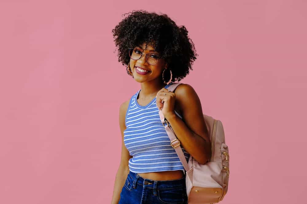 Black girl with long hair wearing casual clothes - blue shirt, jeans, and a pink backpack.
