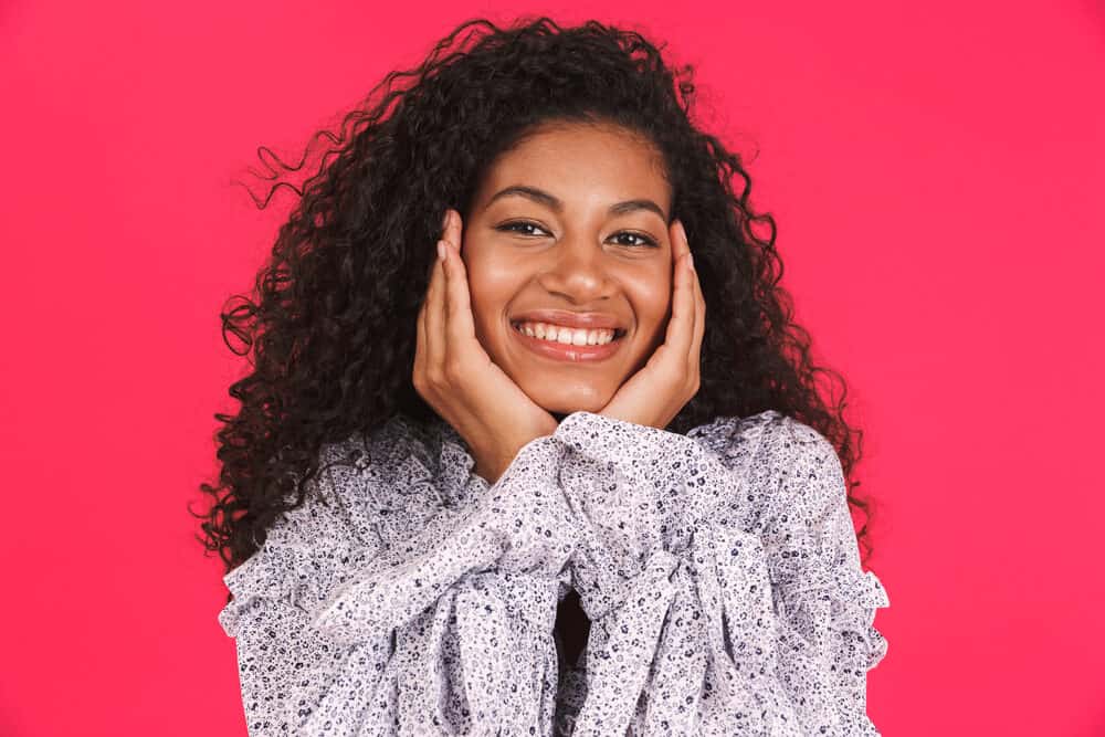 Happy African female with light brown skin wearing a purple dress with bouncy curls created with a round brush.