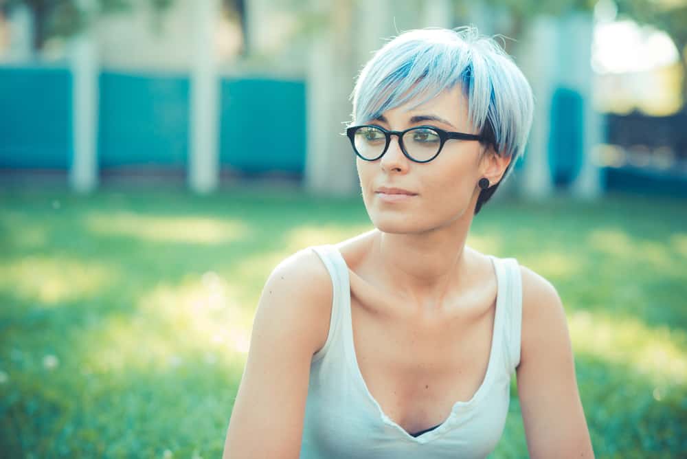 Young female with 1C hair colored with blue hair dye wearing black glasses and a white tank top.