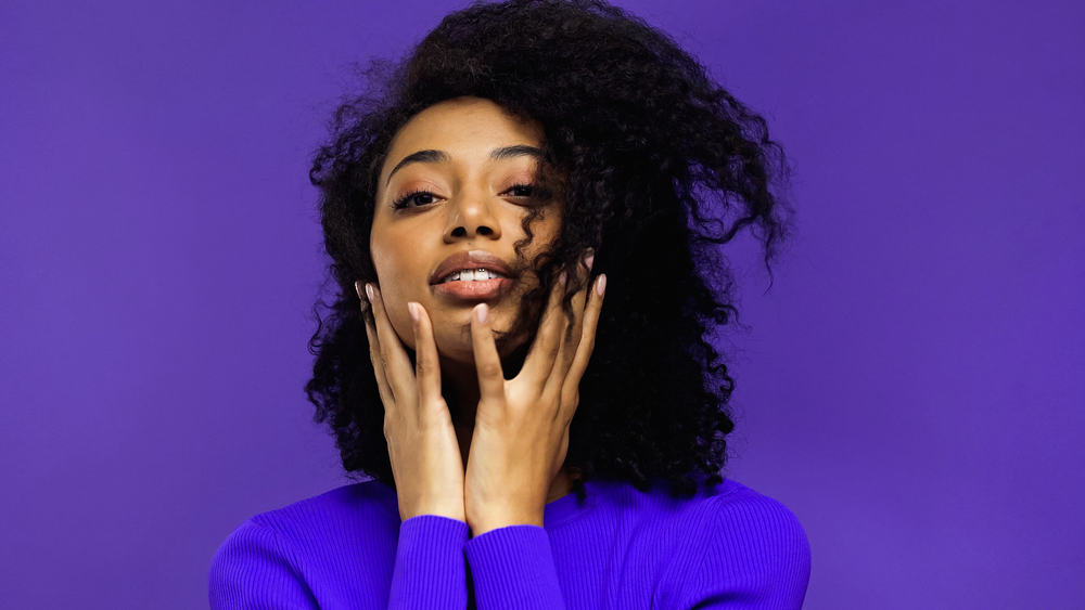 Black lady wearing a purple shirt with an unwanted hair color that's been treated with anti-dandruff shampoo.