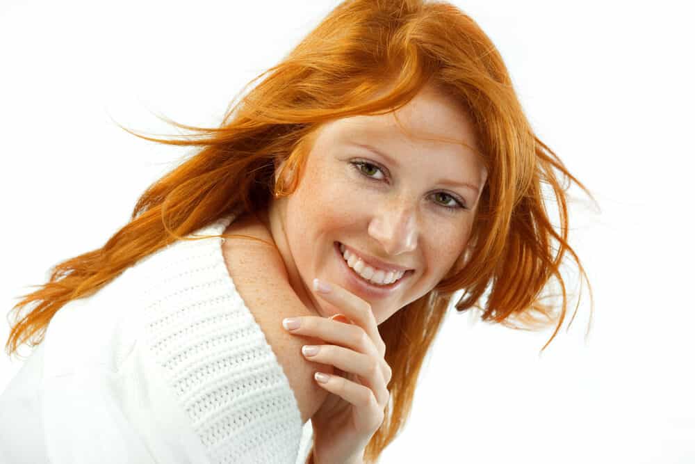 Cute lady with freckles wearing dark ash bleached hair and a white sweater.