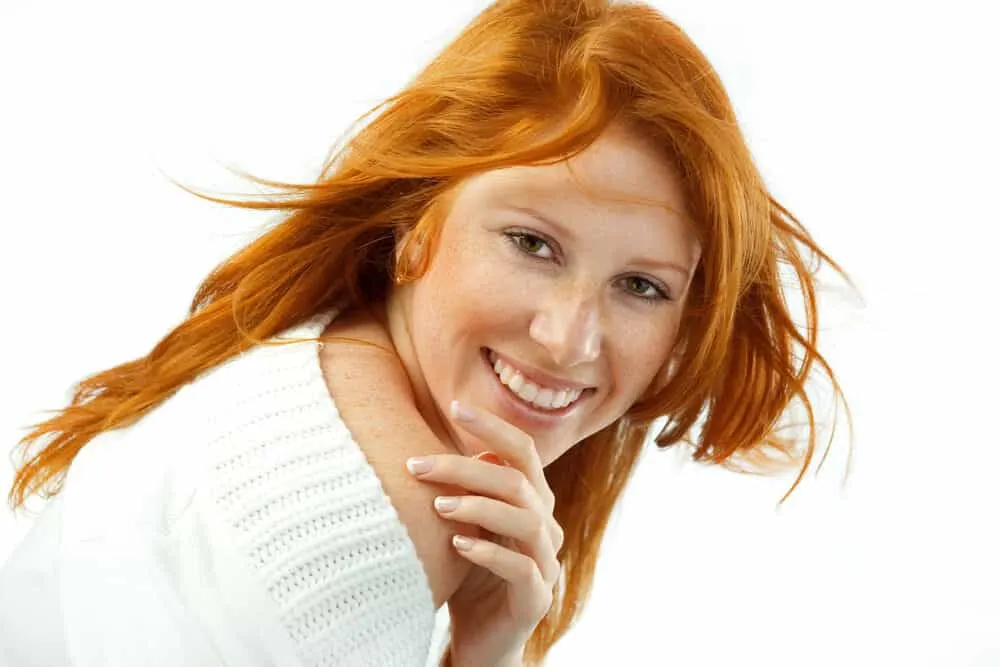 What Color Covers Orange Hair? Brassy? Dye? After Stripping? 4 Cute lady with freckles wearing dark ash bleached hair and a white sweater.