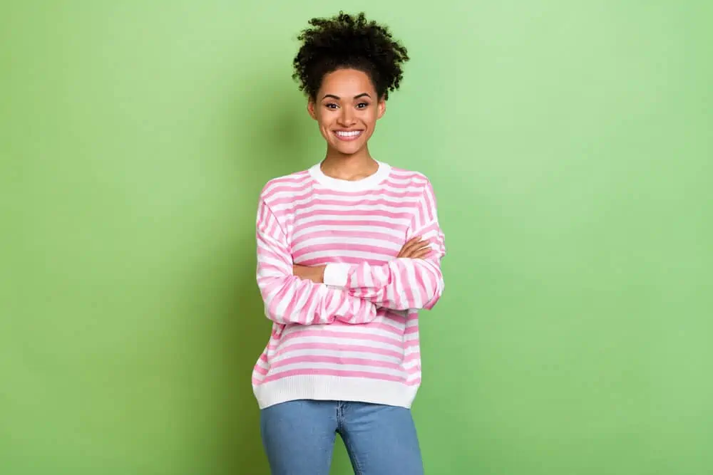 Can You Leave Olaplex 3 on Overnight or Leave It on Too Long? 9 Cute black woman with a curly hair structure wearing casual clothes with her arms folded.
