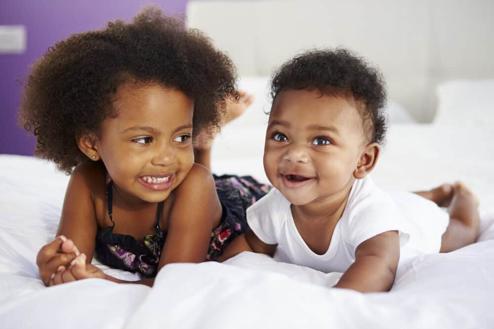 Two cute kids watching other babies on TV. One child is 3 years old and the baby girl is 40 weeks old.