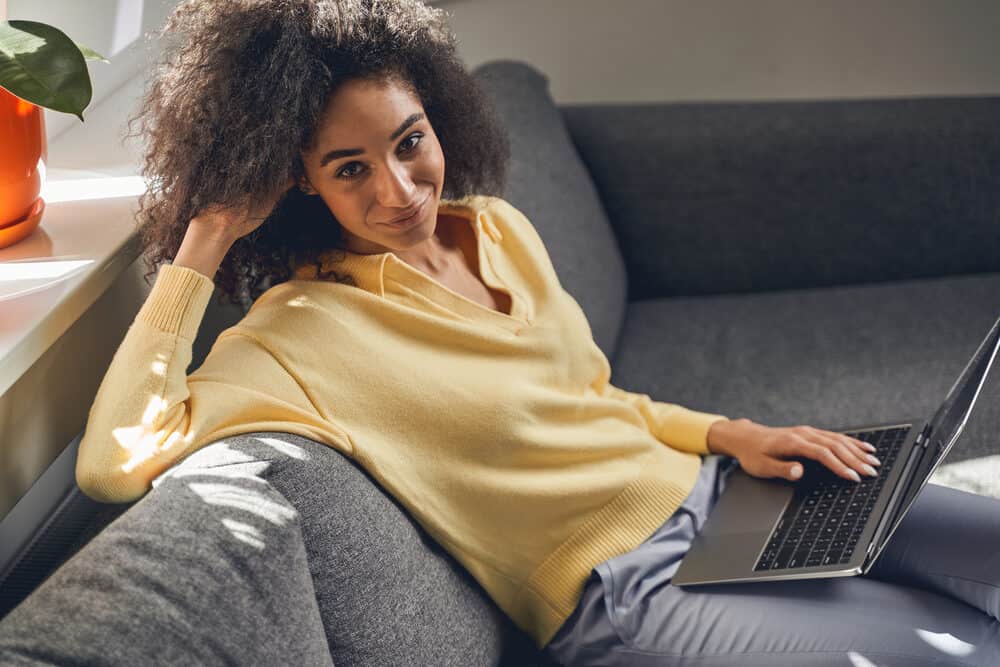 A lady wearing a yellow sweater with fine hair using a laptop to research good hair habits and good hair care tactics.