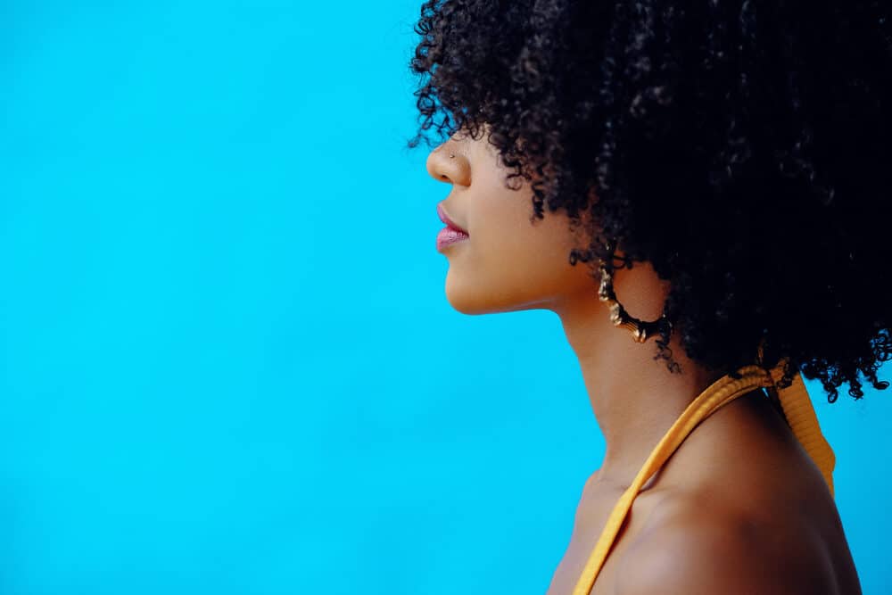 A beautiful black woman with high porosity hair styled with jojoba oil wearing hoop earrings.